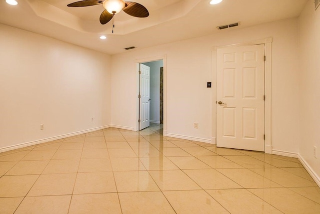 spare room with light tile patterned floors, ceiling fan, and a raised ceiling