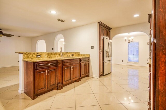 kitchen featuring sink, light stone countertops, ceiling fan with notable chandelier, light tile patterned floors, and stainless steel fridge with ice dispenser