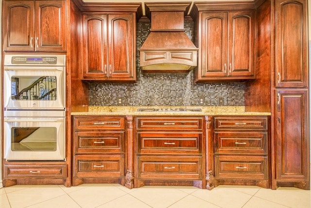 kitchen featuring light stone countertops, premium range hood, double oven, and light tile patterned floors