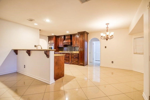 kitchen with a kitchen bar, decorative backsplash, kitchen peninsula, light tile patterned flooring, and stainless steel oven