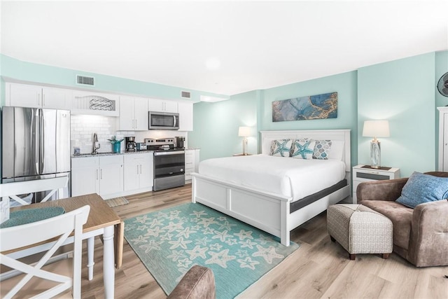 bedroom featuring stainless steel fridge, sink, and light hardwood / wood-style flooring