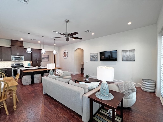 living room featuring visible vents, dark wood-type flooring, baseboards, ceiling fan, and arched walkways