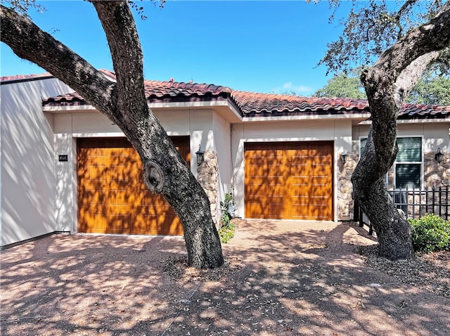 mediterranean / spanish home with a tiled roof, a garage, stone siding, and stucco siding