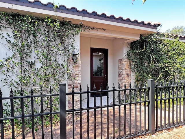 property entrance featuring a tiled roof, stucco siding, and fence