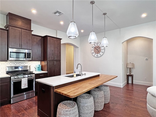 kitchen featuring visible vents, an island with sink, a sink, stainless steel appliances, and dark brown cabinetry