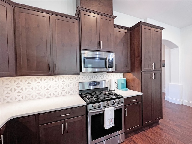 kitchen with dark wood-style floors, stainless steel appliances, light countertops, dark brown cabinetry, and tasteful backsplash