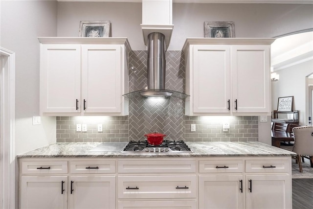 kitchen featuring stainless steel gas cooktop, wall chimney range hood, backsplash, and white cabinets