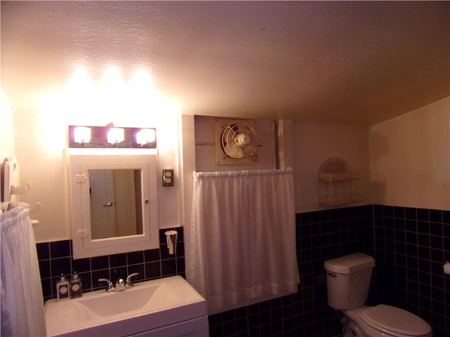 bathroom featuring a textured ceiling, vanity, toilet, and tile walls