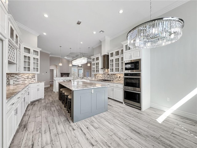 kitchen with arched walkways, ornamental molding, a notable chandelier, appliances with stainless steel finishes, and wall chimney exhaust hood