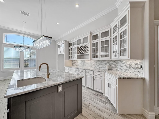 kitchen with ornamental molding, a center island with sink, a sink, backsplash, and white cabinetry