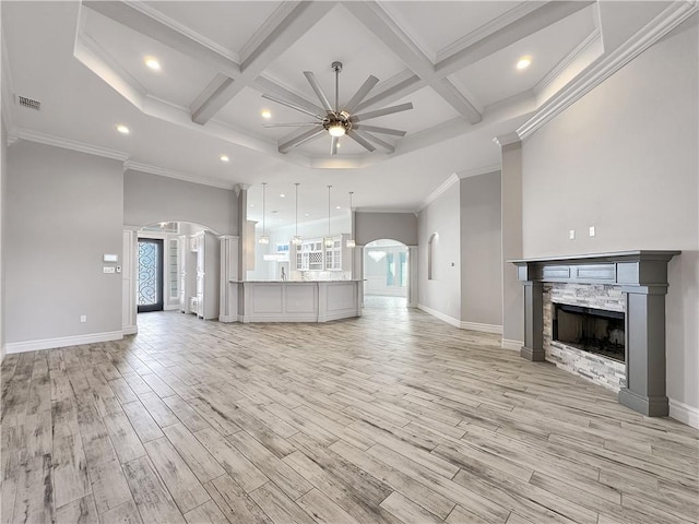 unfurnished living room with visible vents, arched walkways, a stone fireplace, a towering ceiling, and light wood-type flooring