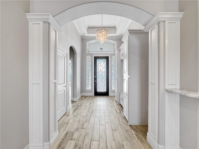 entrance foyer featuring arched walkways, ornamental molding, a raised ceiling, light wood-type flooring, and a chandelier