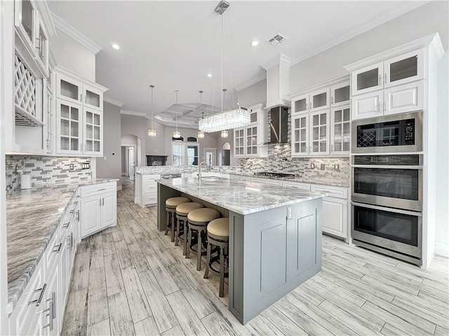 kitchen featuring visible vents, wall chimney range hood, appliances with stainless steel finishes, arched walkways, and a sink