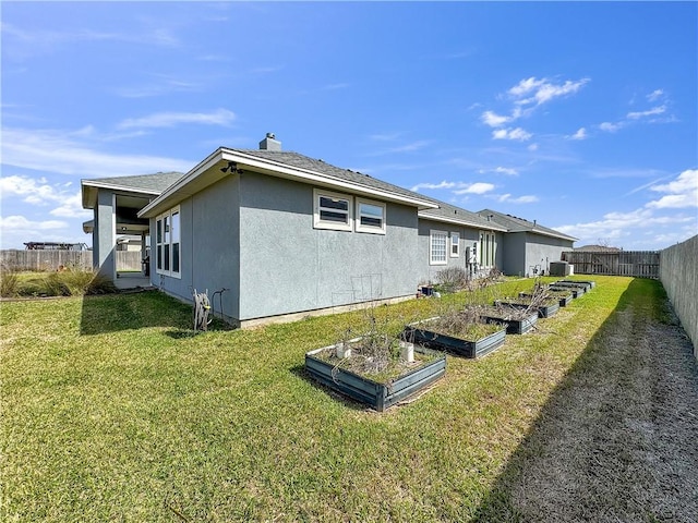 back of house with a garden, a yard, fence private yard, and stucco siding