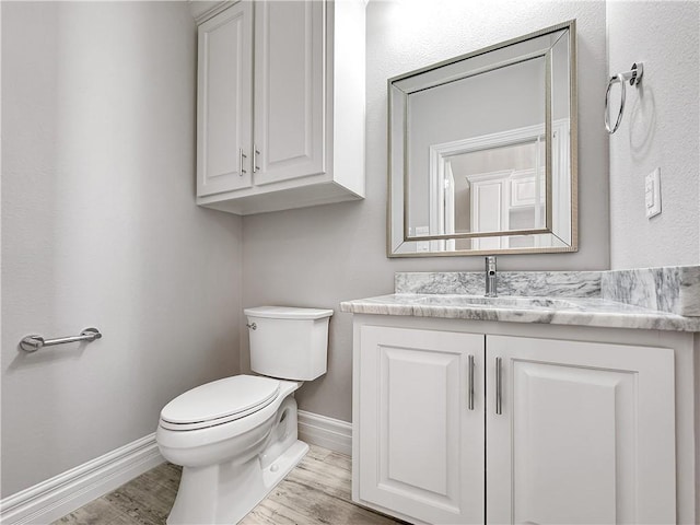 half bathroom featuring baseboards, toilet, wood finished floors, and vanity