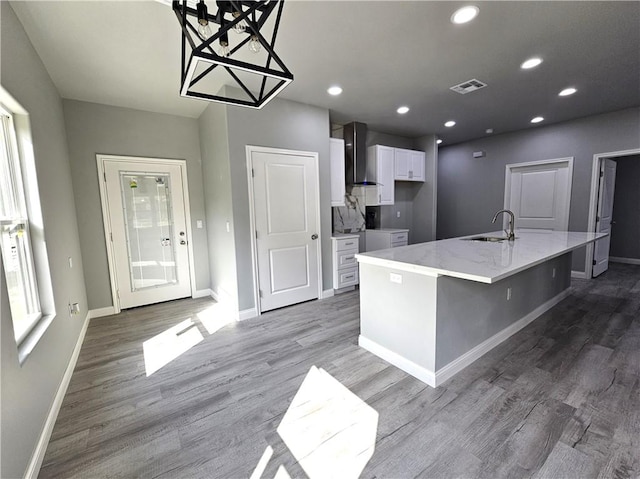 kitchen with wall chimney range hood, white cabinets, a sink, baseboards, and visible vents