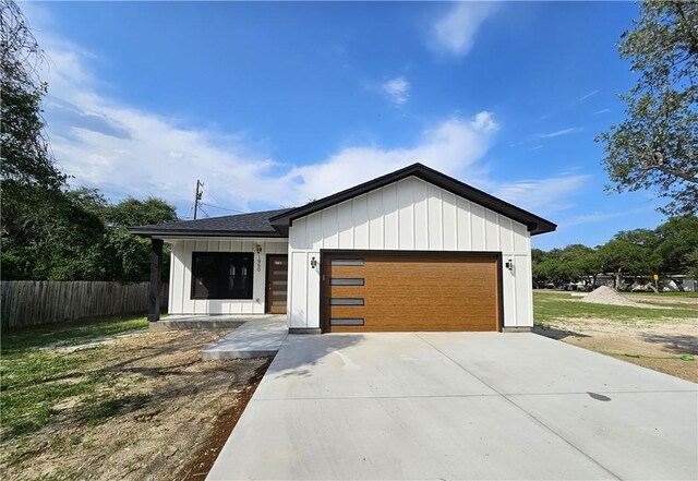 view of front of house with an attached garage, board and batten siding, fence, and driveway