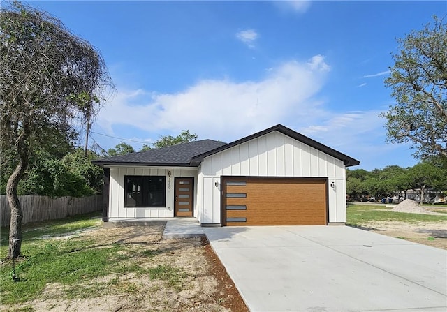 view of front facade featuring fence, an attached garage, a shingled roof, board and batten siding, and driveway
