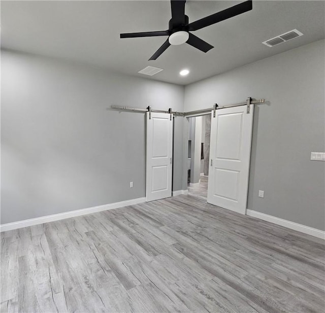 unfurnished bedroom with visible vents, a barn door, baseboards, and wood finished floors