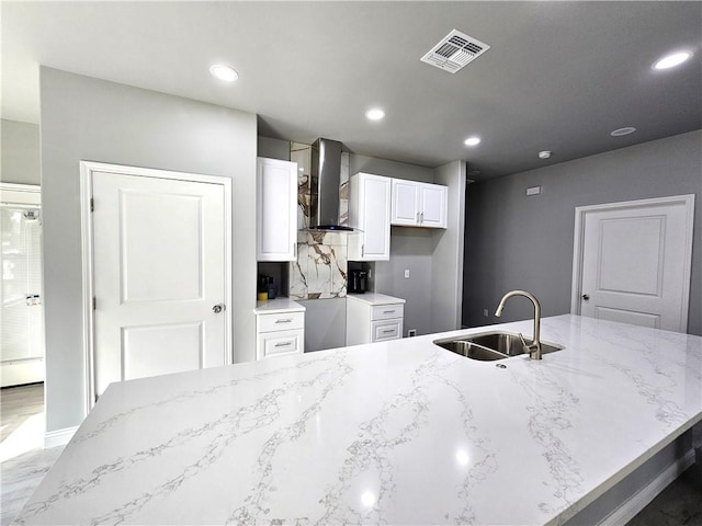 kitchen with visible vents, a sink, wall chimney range hood, and light stone countertops
