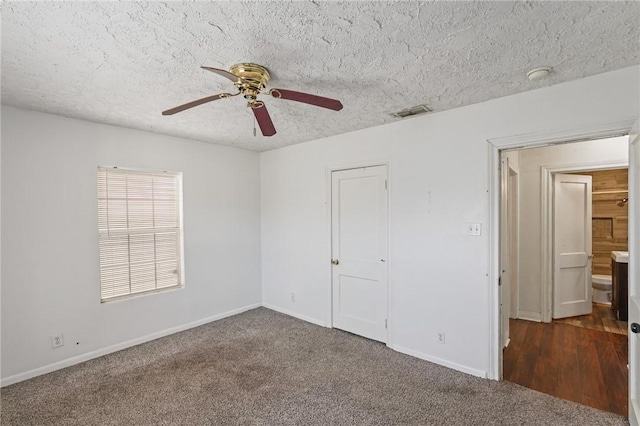 unfurnished bedroom featuring dark colored carpet, ceiling fan, ensuite bathroom, and a textured ceiling