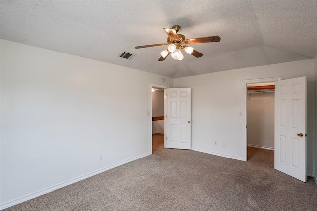 unfurnished bedroom with carpet floors, a walk in closet, lofted ceiling, visible vents, and baseboards