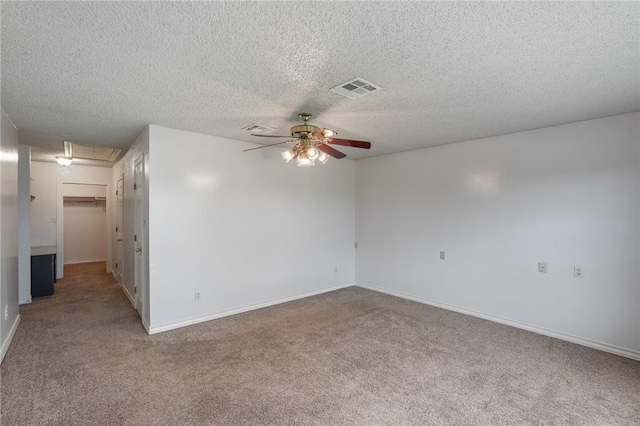 carpeted spare room with attic access, baseboards, visible vents, ceiling fan, and a textured ceiling