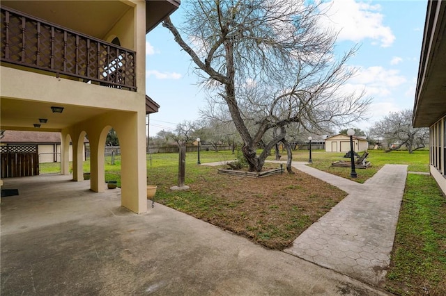 view of yard featuring a patio, a balcony, a storage shed, an outdoor structure, and fence