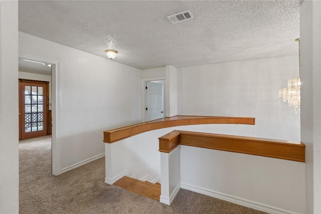 corridor featuring a textured ceiling, carpet flooring, visible vents, baseboards, and an inviting chandelier