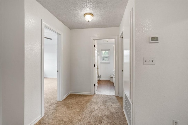 hallway featuring light carpet, baseboards, a textured ceiling, and a textured wall