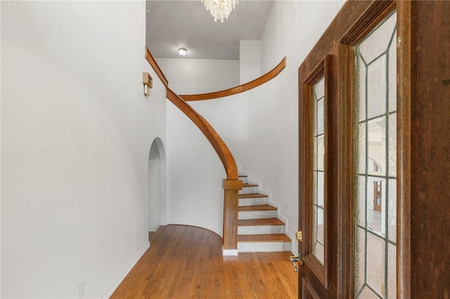 foyer featuring arched walkways, a notable chandelier, baseboards, stairway, and light wood-type flooring