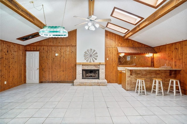 unfurnished living room featuring light tile patterned floors, vaulted ceiling with skylight, wood walls, and a fireplace