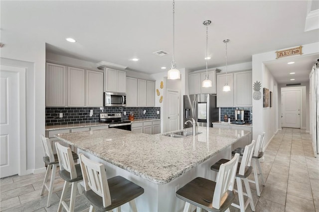 kitchen with light stone countertops, sink, a spacious island, decorative light fixtures, and appliances with stainless steel finishes