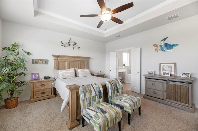 bedroom featuring ceiling fan, ensuite bathroom, crown molding, light colored carpet, and a tray ceiling