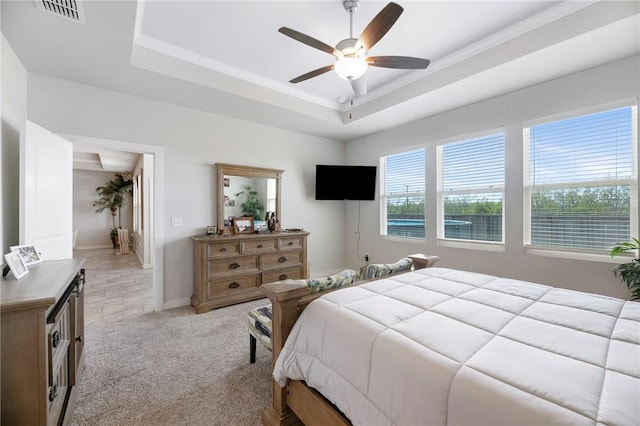 bedroom with ceiling fan, light colored carpet, and a tray ceiling