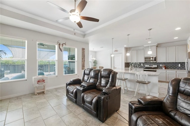 tiled living room with a tray ceiling, ceiling fan, crown molding, and sink