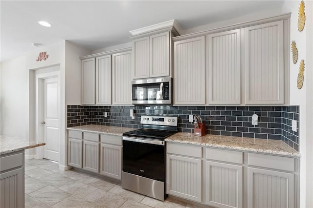 kitchen featuring gray cabinetry, decorative backsplash, light stone counters, and appliances with stainless steel finishes