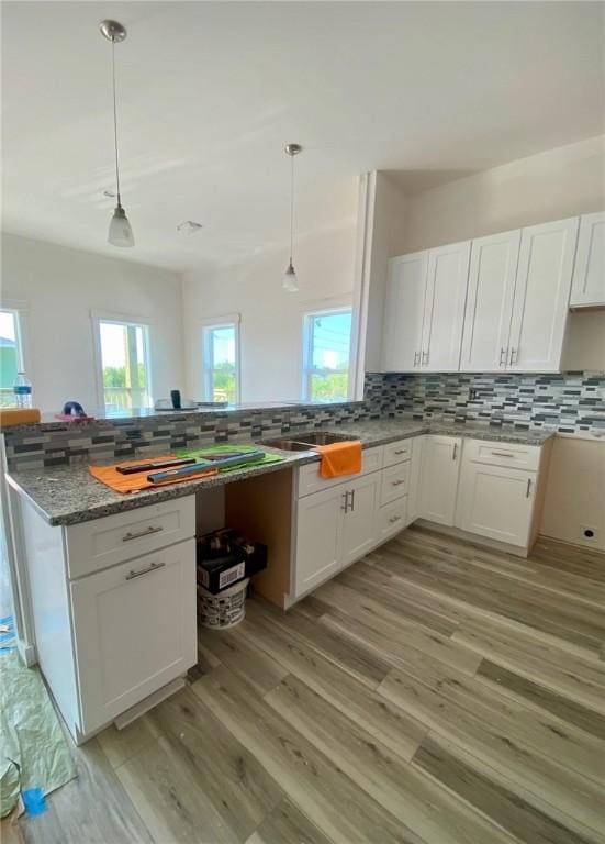kitchen featuring light wood-style flooring, backsplash, white cabinets, and hanging light fixtures