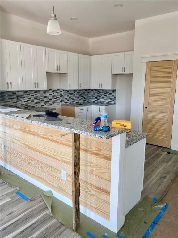 kitchen featuring white cabinets, stone countertops, wood finished floors, hanging light fixtures, and backsplash