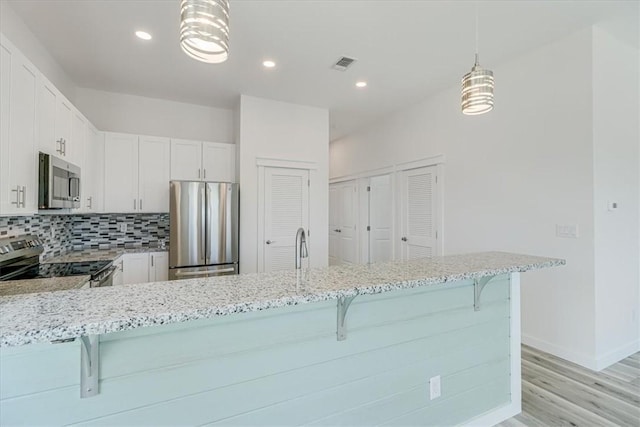 235 Port Mansfield St, Port Aransas, TX 78373 - kitchen featuring stainless steel appliances, light stone counters, light wood-style flooring, a kitchen breakfast bar, and recessed lighting