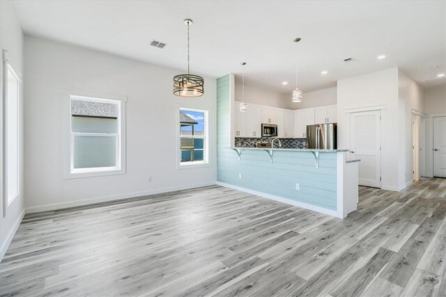 235 Port Mansfield St, Port Aransas, TX 78373 - kitchen with stainless steel appliances, a peninsula, a kitchen breakfast bar, light wood-style flooring, and white cabinets