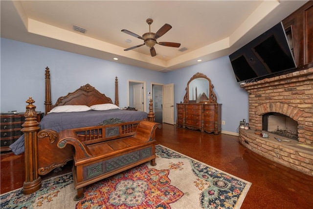 bedroom featuring a tray ceiling, ceiling fan, and a large fireplace