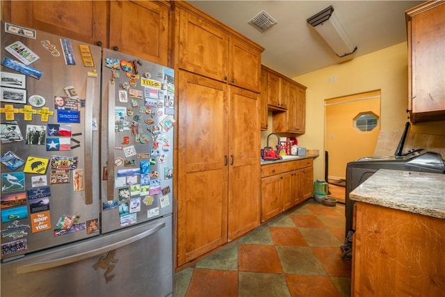 kitchen featuring light stone countertops, stainless steel refrigerator, and sink