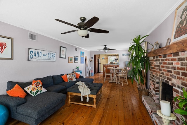 living room with ceiling fan, wood-type flooring, a fireplace, and crown molding