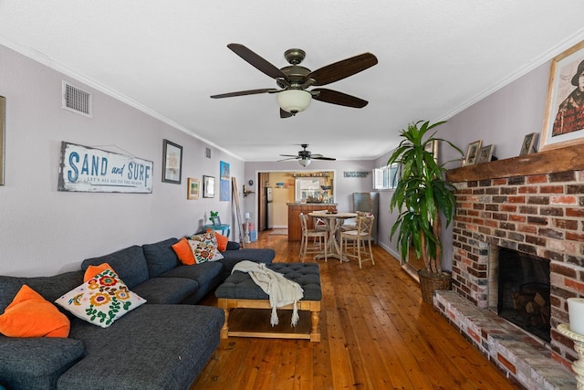 living room featuring a brick fireplace, hardwood / wood-style flooring, ceiling fan, and ornamental molding