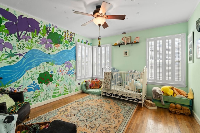 bedroom featuring hardwood / wood-style floors, a nursery area, and ceiling fan