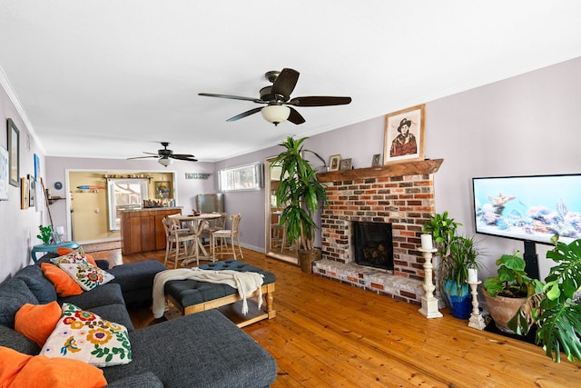 living room with a brick fireplace, hardwood / wood-style flooring, ceiling fan, and crown molding