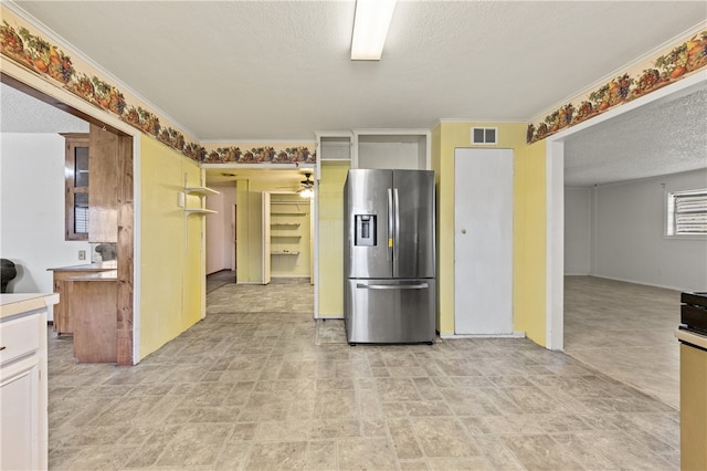 kitchen with a textured ceiling, ornamental molding, ceiling fan, white cabinetry, and stainless steel fridge