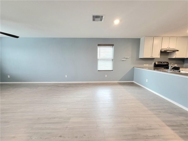 interior space featuring white cabinets, stainless steel range oven, light wood-type flooring, and sink