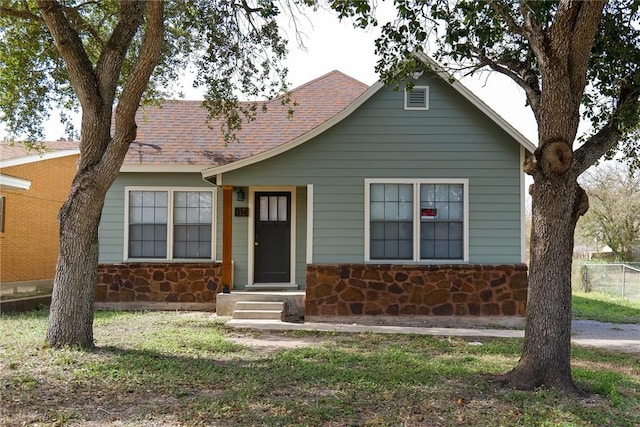 view of front of house with stone siding, fence, and roof with shingles